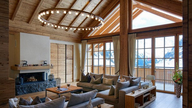 A cozy living room with a fireplace, sofas, and a large window with a mountain view. - Arlberg Hospiz Chalet Suiten (Sankt Anton am Arlberg)