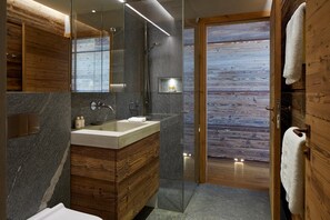 Een moderne badkamer met een houten wastafelmeubel, een glazen douchecabine en een houten vloer.