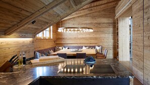 A wooden interior with a dining area, a kitchen with a marble countertop, and a hanging light fixture. - Arlberg Hospiz Chalet Suiten (Sankt Anton am Arlberg)