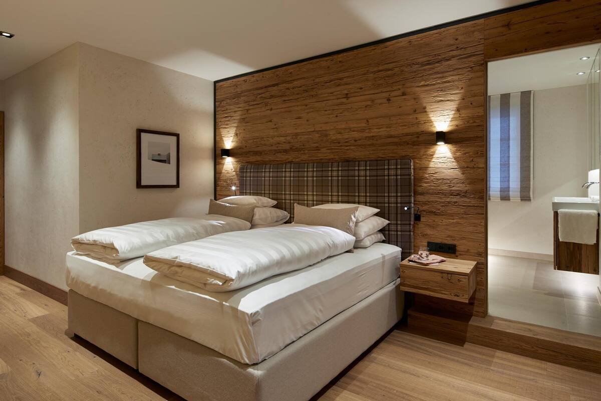 Ein modernes Schlafzimmer mit einem großen Bett, einer Wand aus Holzpaneelen und einem durch eine Glastür einsehbaren Badezimmer.