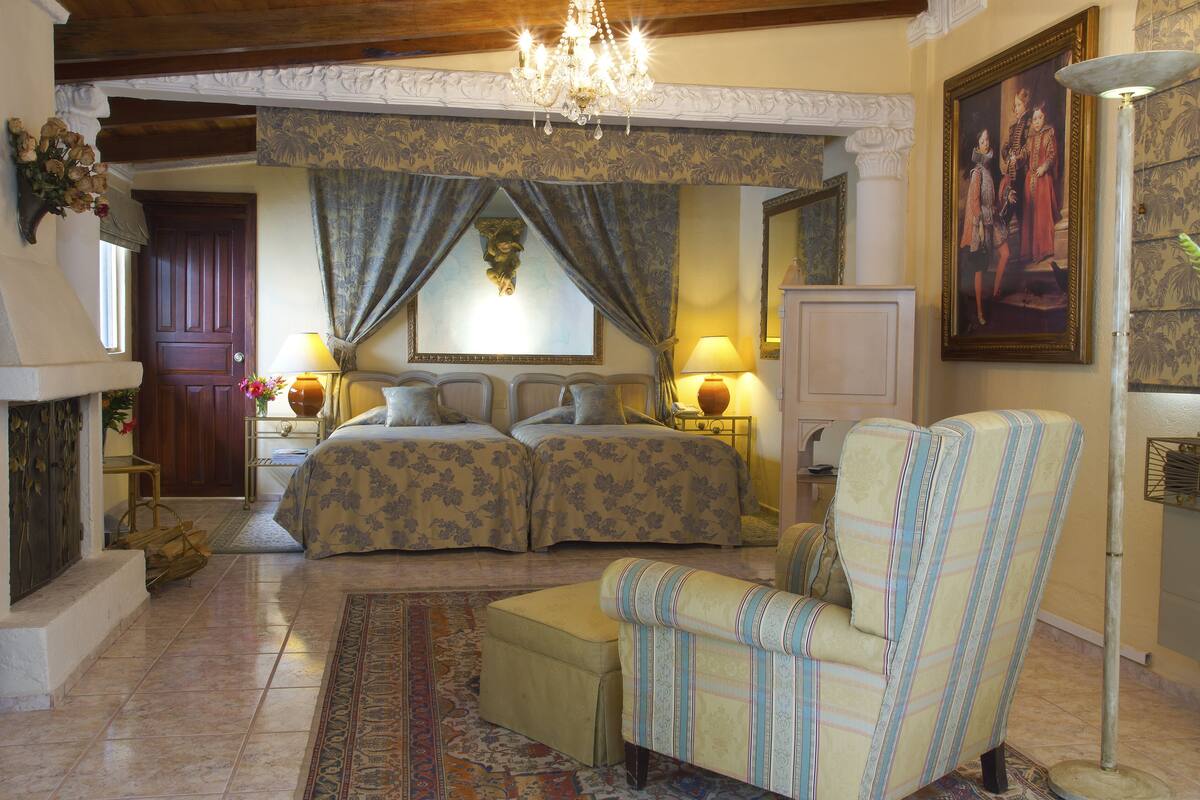Quarto com duas camas, um candelabro, um quadro grande e um tapete estampado.