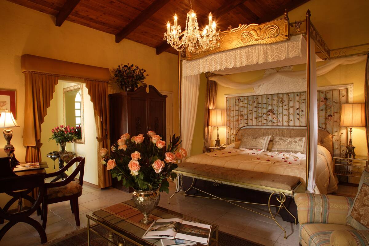 Quarto com cama de dossel, um candelabro e um vaso de flores sobre uma mesa.