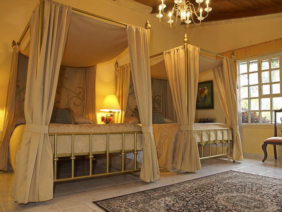 Una cama con dosel y cortinas, un candelabro y vistas del exterior a través de una ventana.