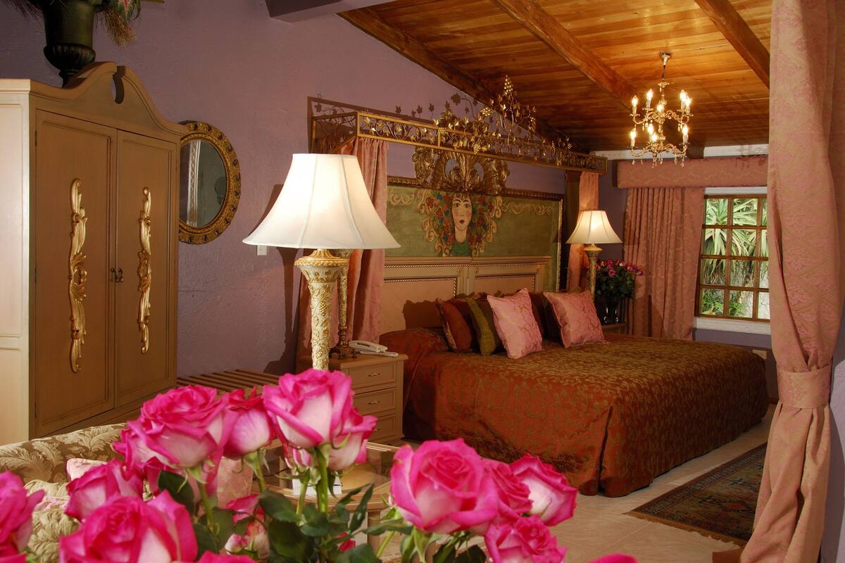 Quarto com uma cama grande, duas mesas de cabeceira, cômoda e um lustre.
