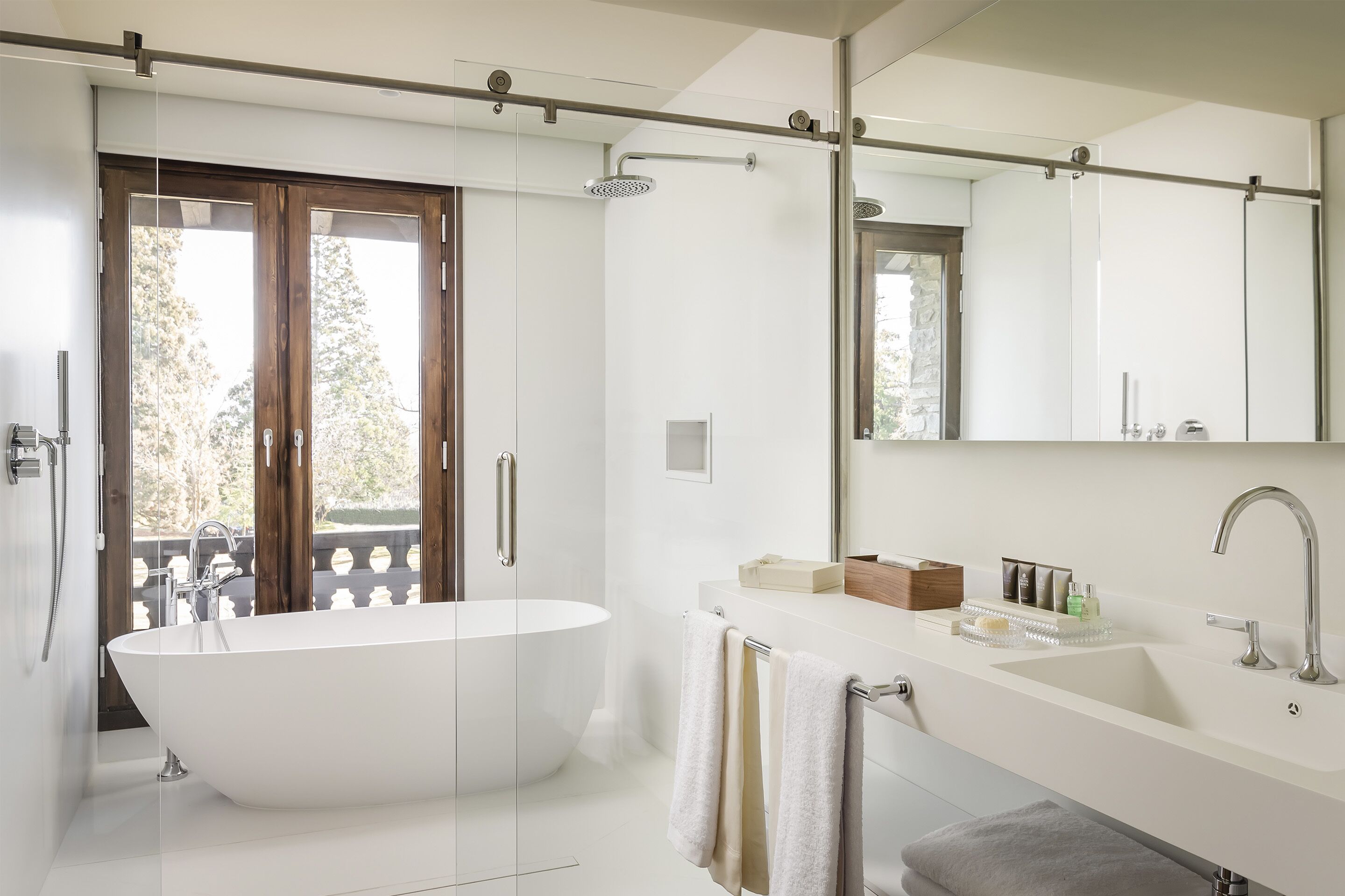 Een moderne badkamer met een vrijstaand bad, een grote spiegel en een douchekop.
