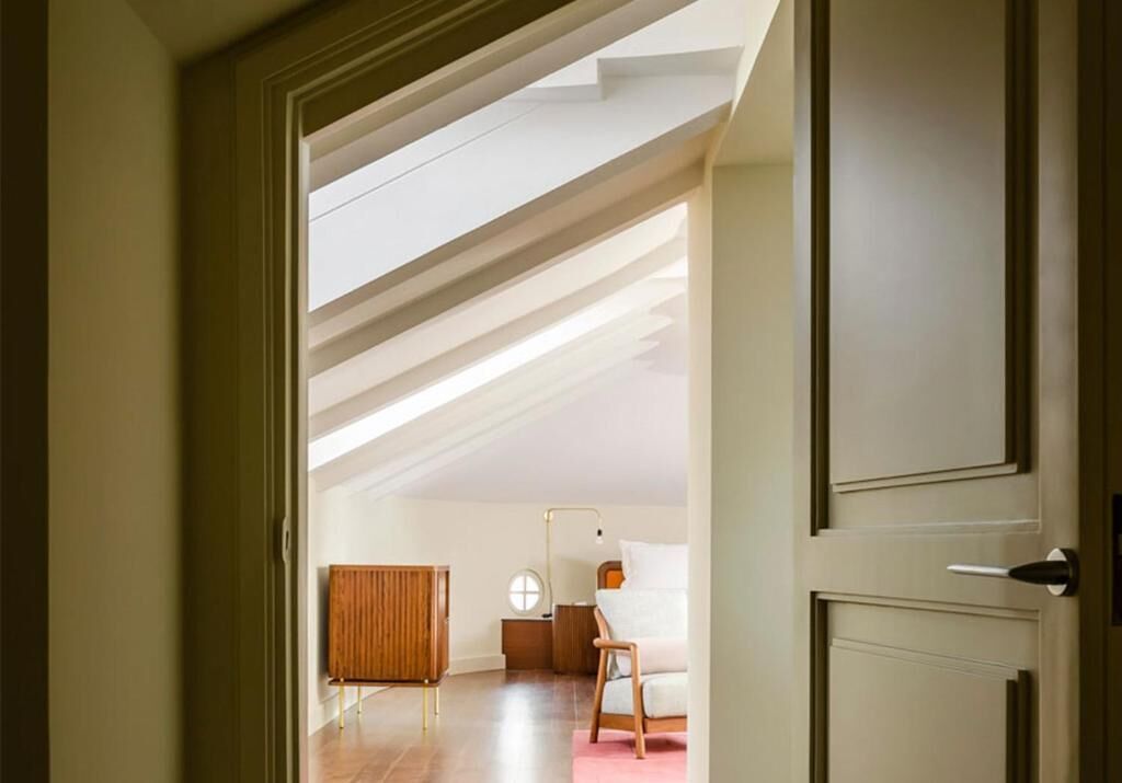 An attic bedroom with a sloped ceiling, a bed, a bedside table, and a wardrobe.