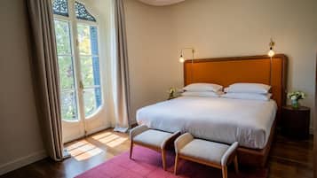A bedroom with a large bed, a bench, a nightstand, and a window with curtains.