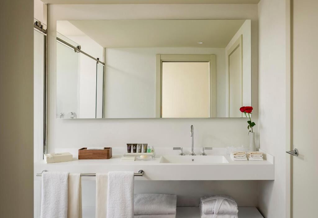 A modern bathroom with a large mirror, two sinks, and a shower.