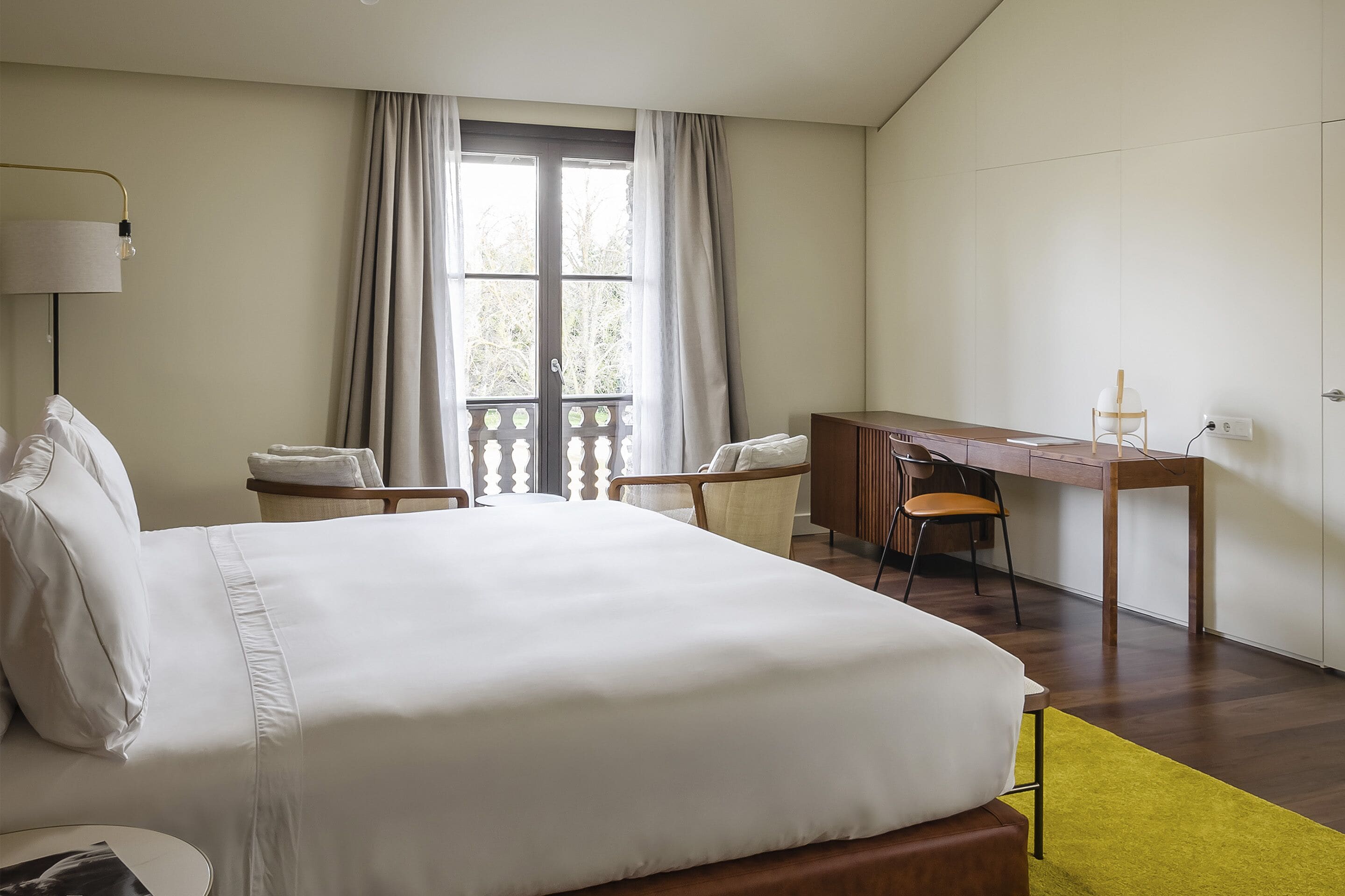 Una habitación de hotel con una cama grande, un escritorio, dos sillas y una ventana con cortinas.