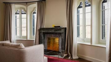 Una habitación con chimenea, sofá y ventanas grandes con cortinas.
