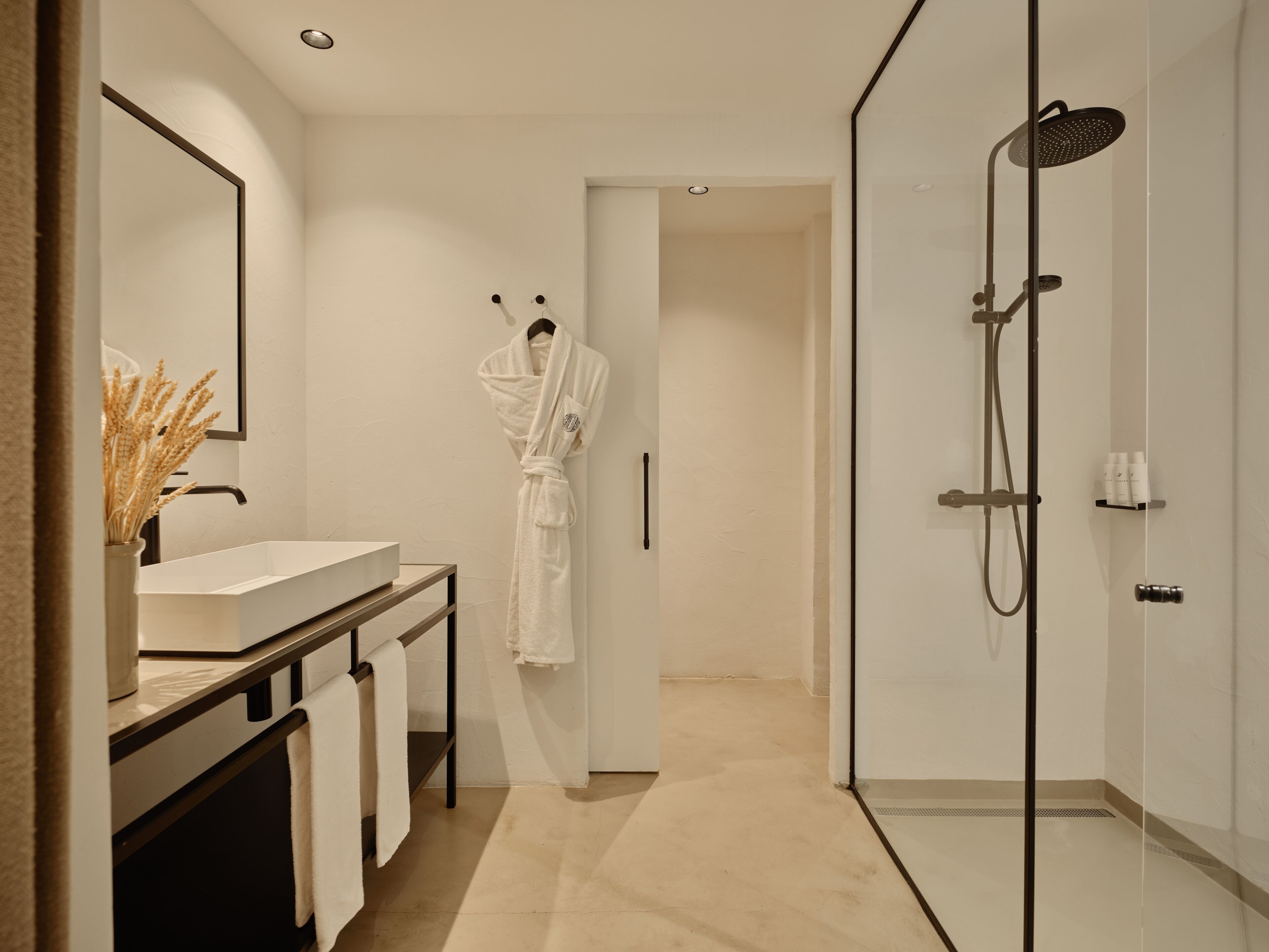 Un baño moderno con ducha de vidrio, un lavamanos blanco y una bata colgada en la pared.