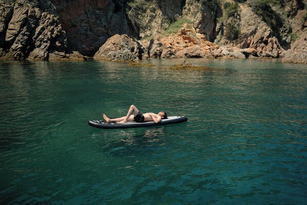 A person lying on a floating device in a body of water with rocky cliffs in the background. - Mas de Torrent Hotel & Spa, Relais & Châteaux (Torrent)