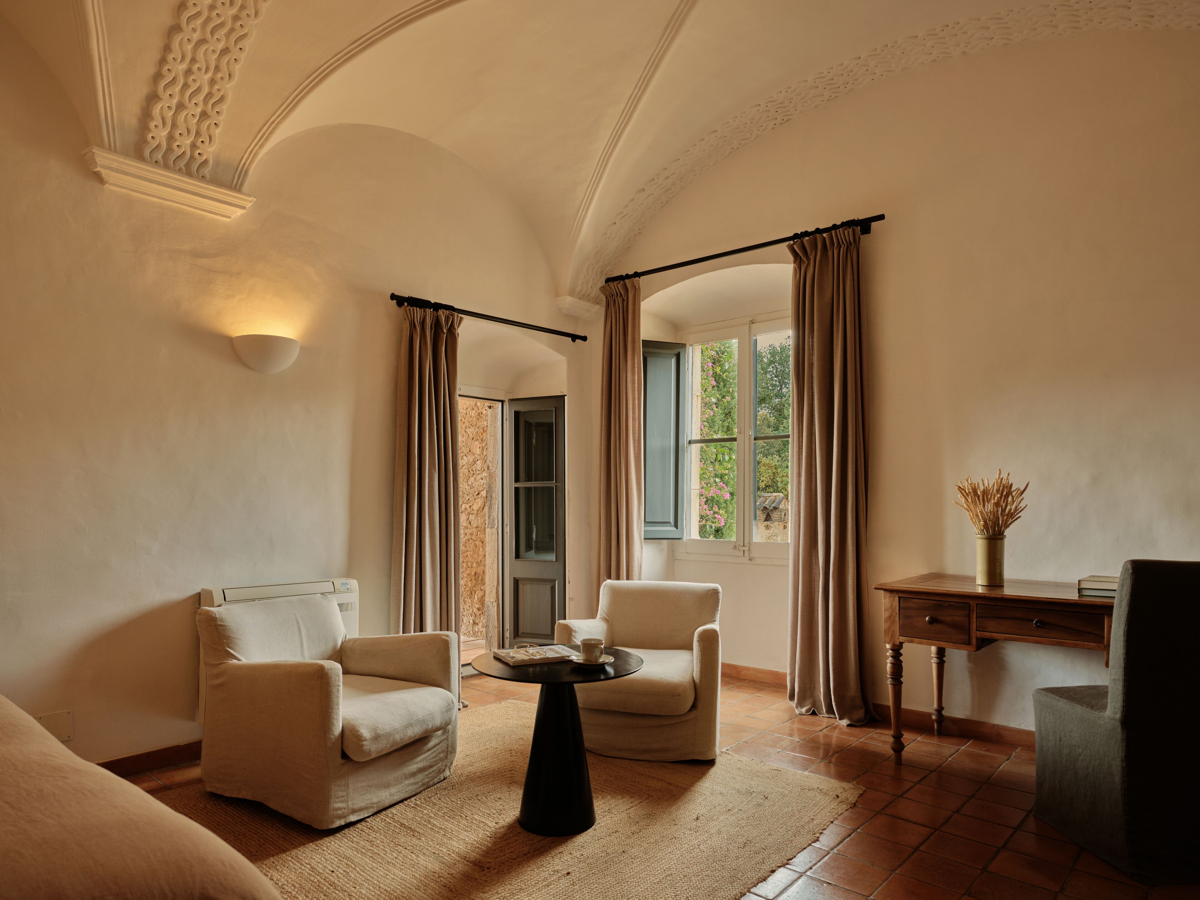 A room with two armchairs, a small round table, a desk with a vase, and a window with curtains.