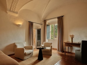 A room with two armchairs, a small round table, a desk with a vase, and a window with curtains. - Mas de Torrent Hotel & Spa, Relais & Châteaux (Torrent)