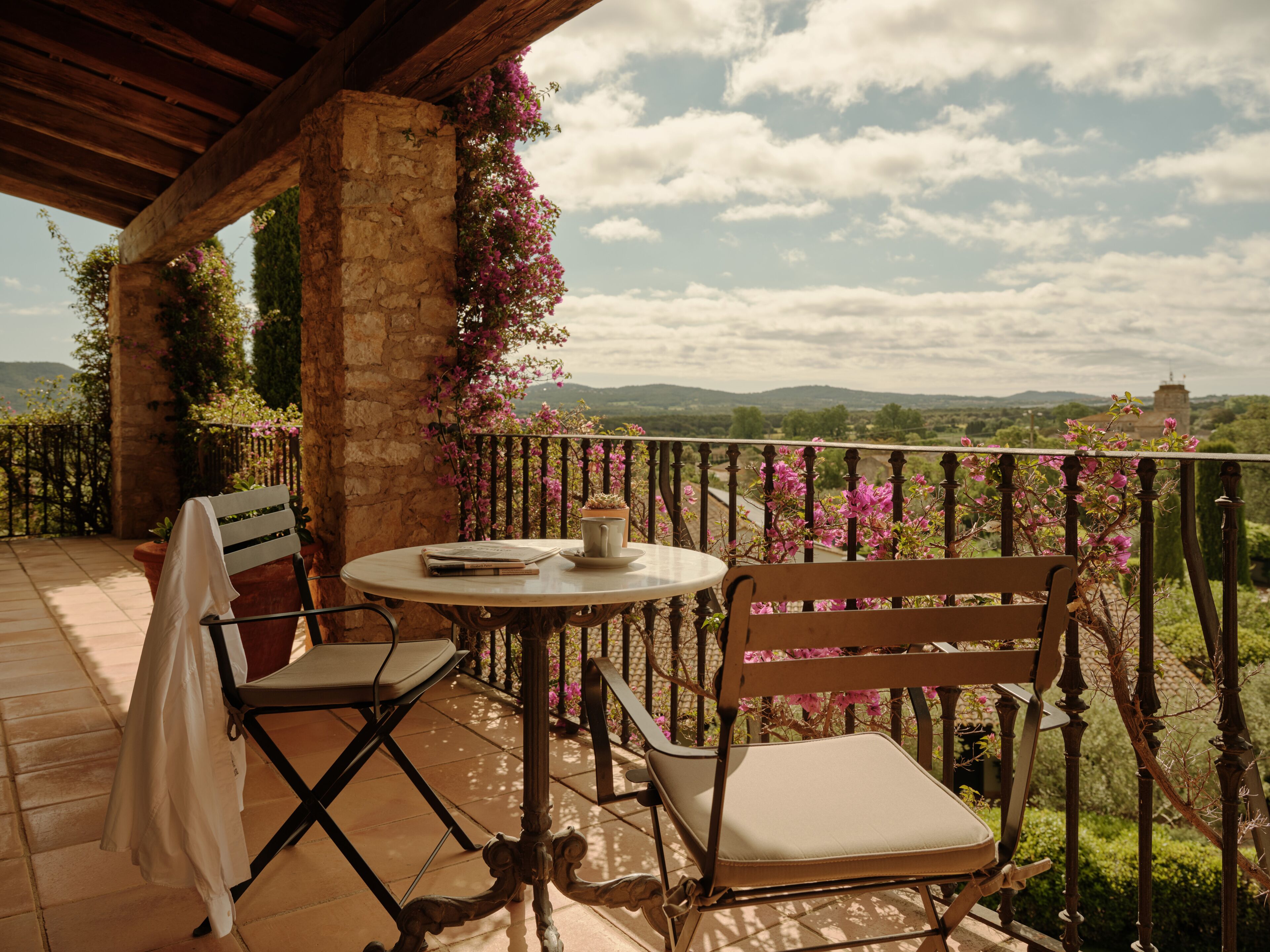 A balcony with a table and chairs, a potted plant, and a view of the countryside.