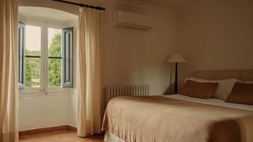 Un dormitorio con cama, ventana con cortinas, radiador y lámpara.