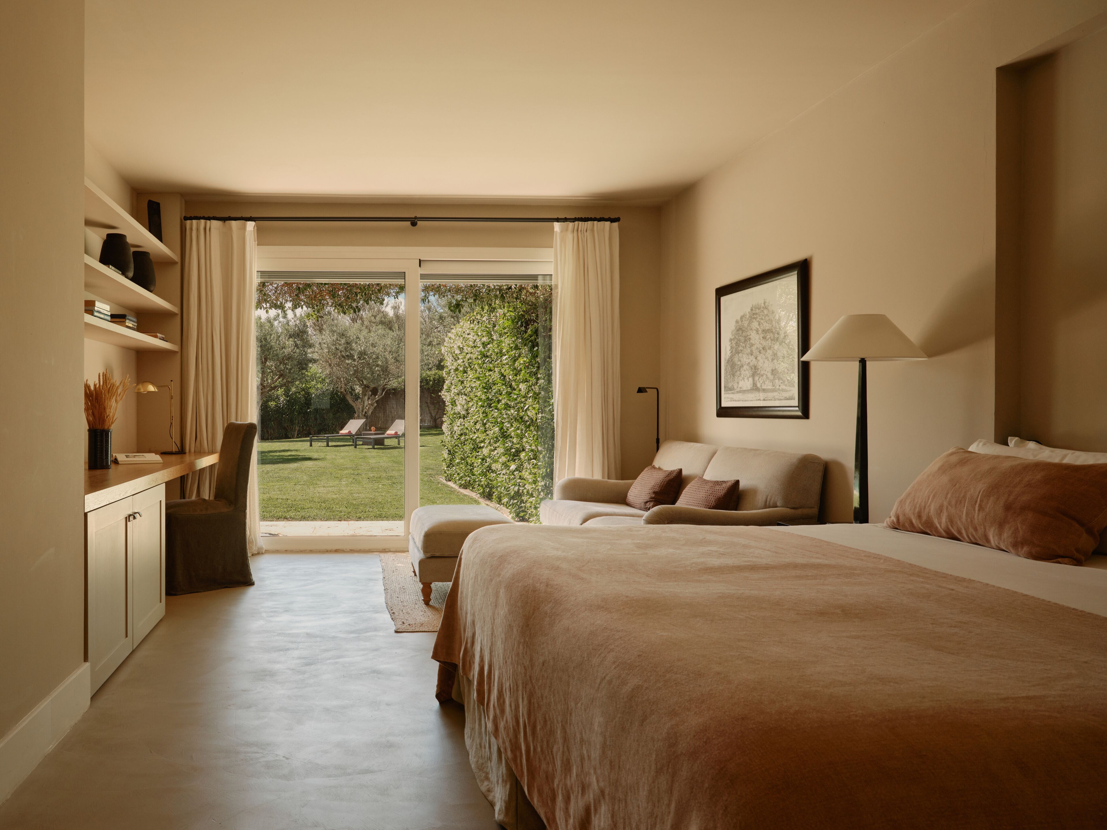 A bedroom with a bed, a sofa, a desk, and a view of the garden.