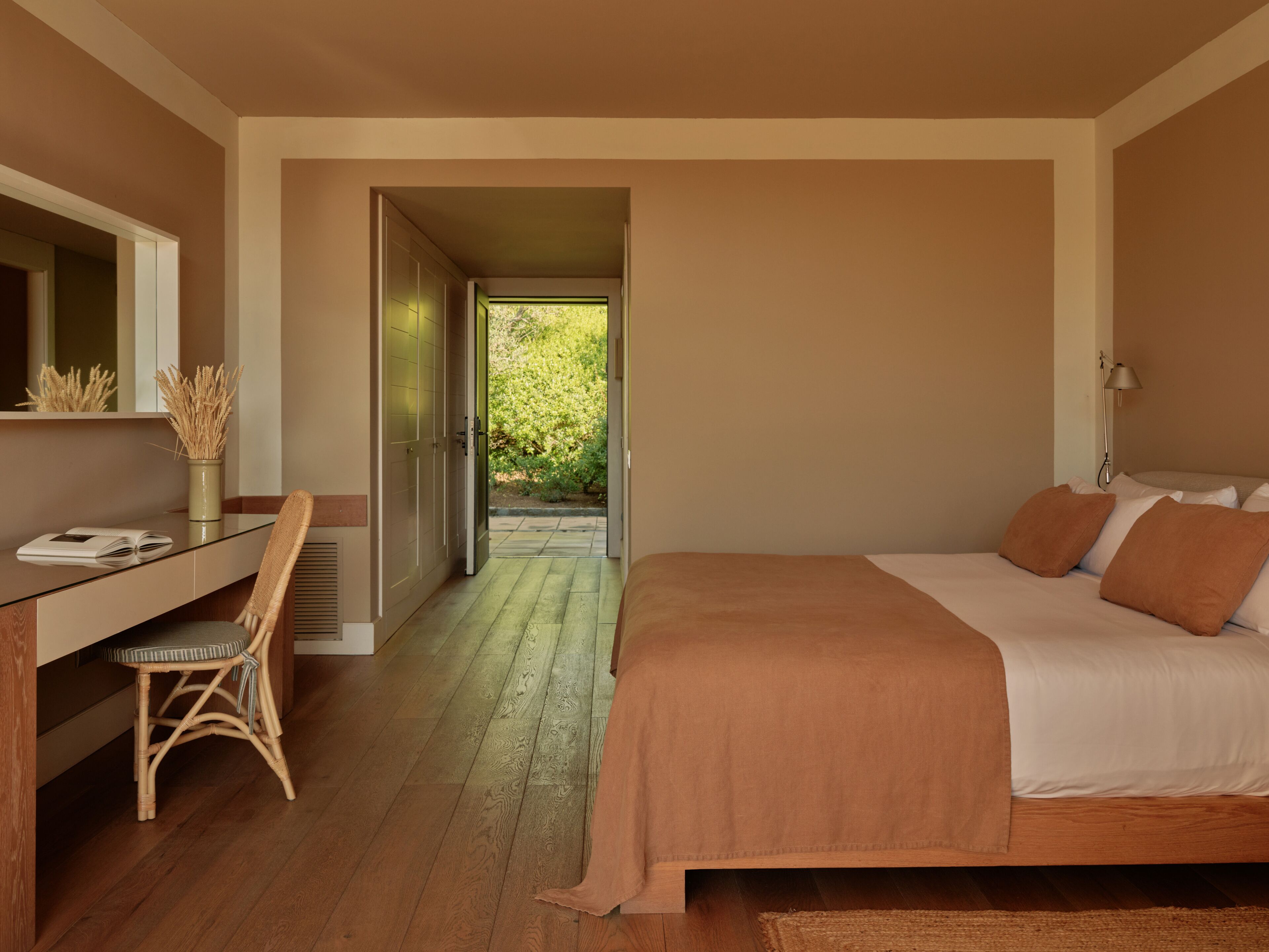 Un dormitorio con cama, escritorio y silla. Se ve una puerta que da a un jardín.