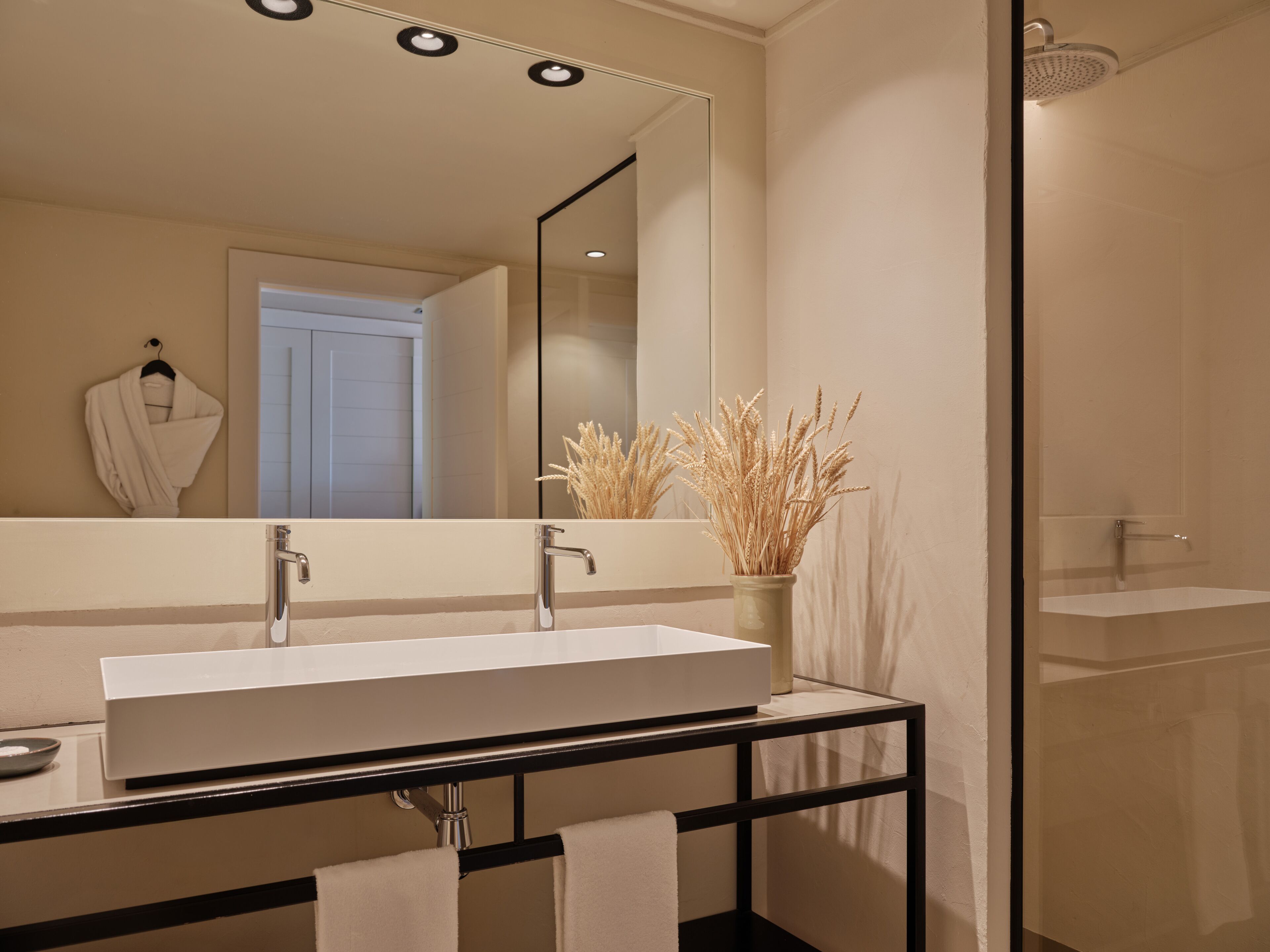 Un baño moderno con un espejo grande, un lavabo blanco y una cabina de ducha con mampara de vidrio.