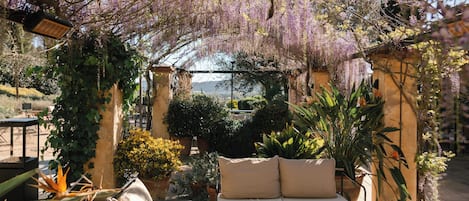 An outdoor seating area with a sofa and table, surrounded by potted plants and a view of the landscape.