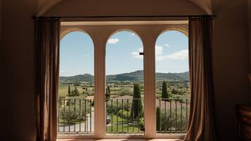 Una habitación con vistas a través de una ventana de tres arcos, un balcón con barandilla de metal y piso de baldosas.
