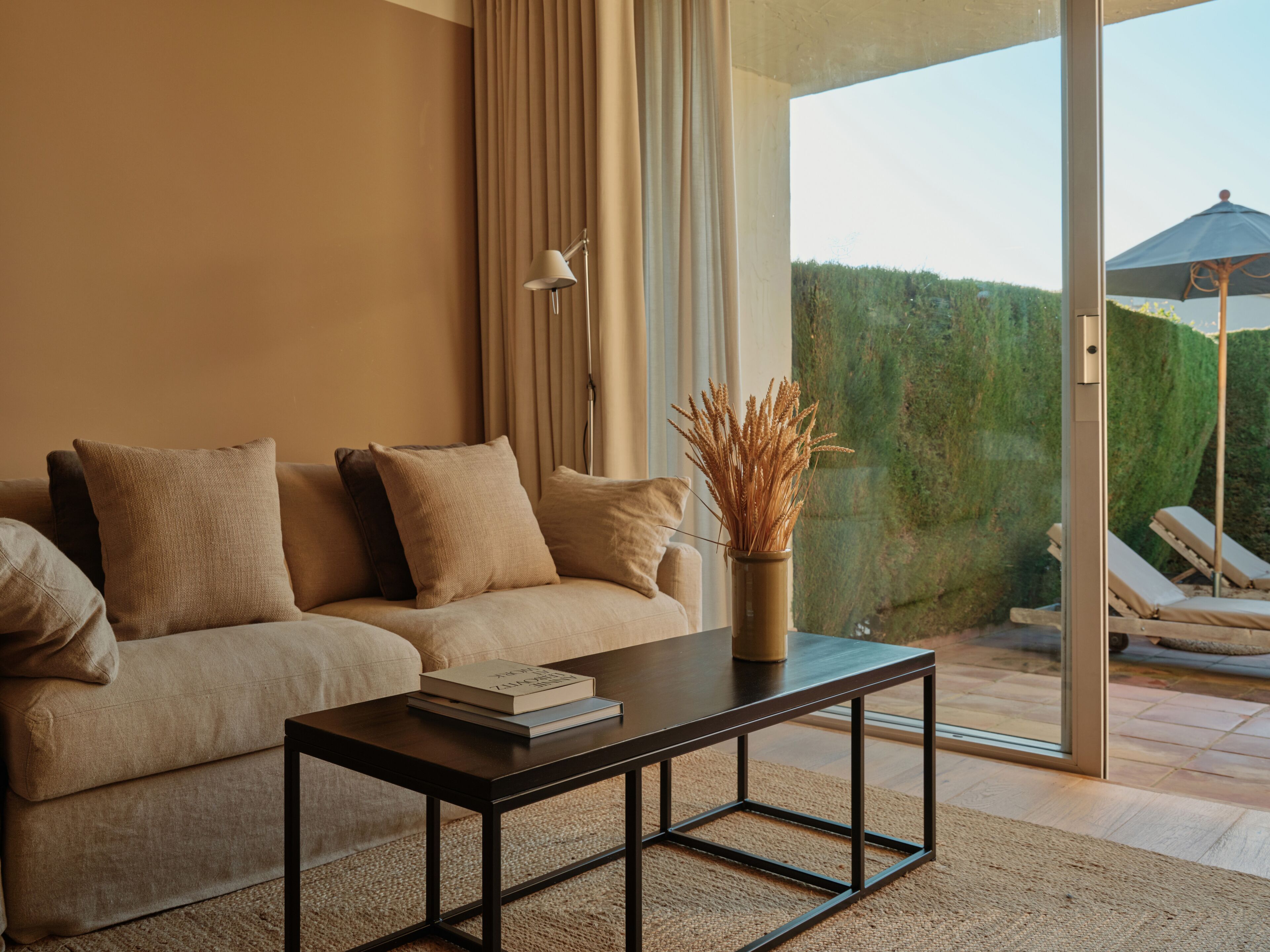 A modern living room with a sofa, a coffee table, and a view of a garden through a glass door.