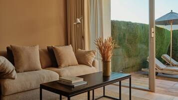 A modern living room with a sofa, a coffee table, and a view of a garden through a glass door.