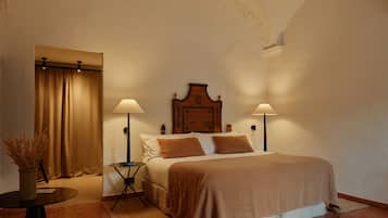 A bedroom with a bed, two bedside lamps, a nightstand, a vase with dried plants, and a curtain.