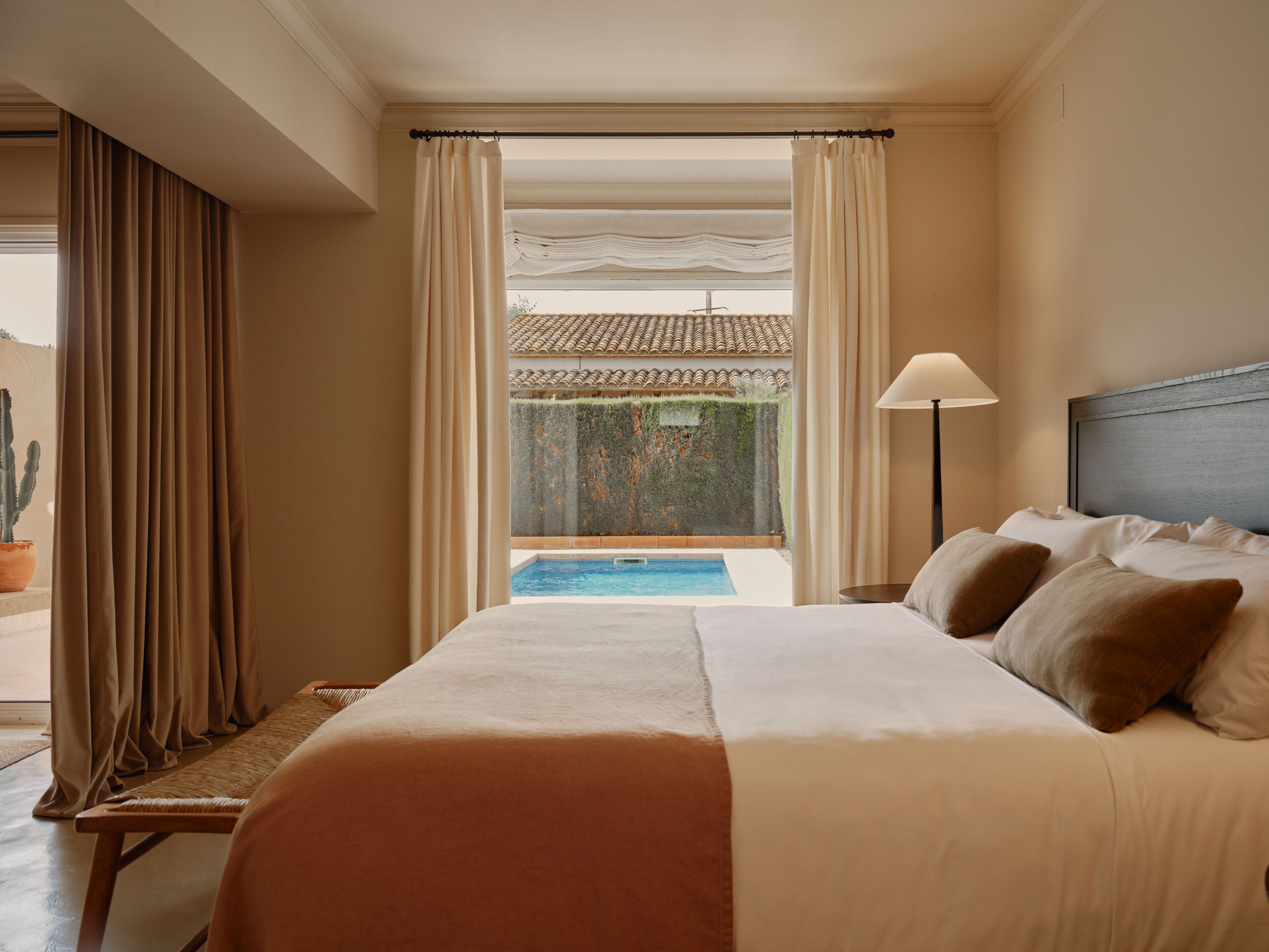 Une chambre d’hôtel avec un lit, une lampe de chevet, une vue sur une piscine et un cactus à l’extérieur.