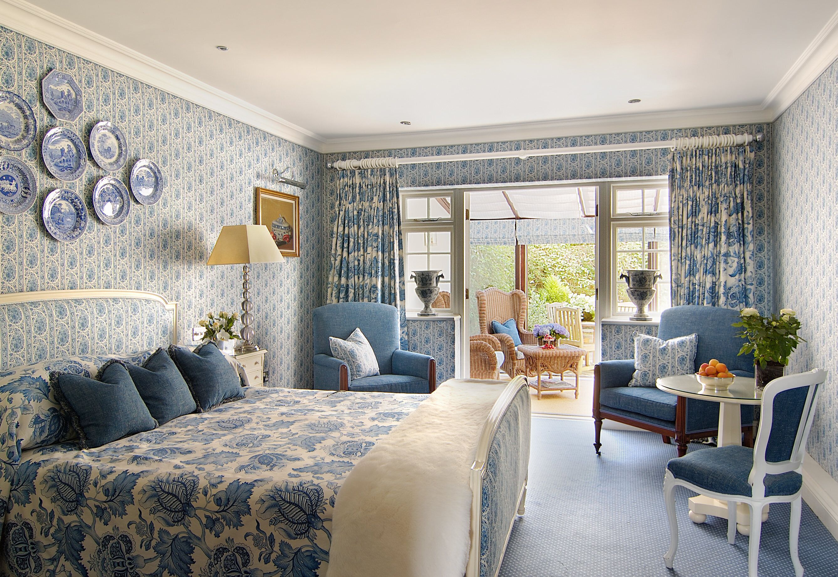 A bedroom with a large bed, two armchairs, a small table, and a window with curtains.