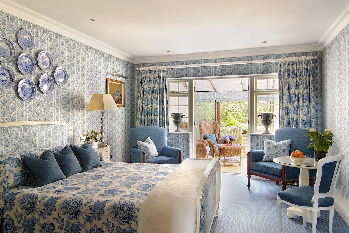 A bedroom with a large bed, two armchairs, a small table, and a window with curtains.