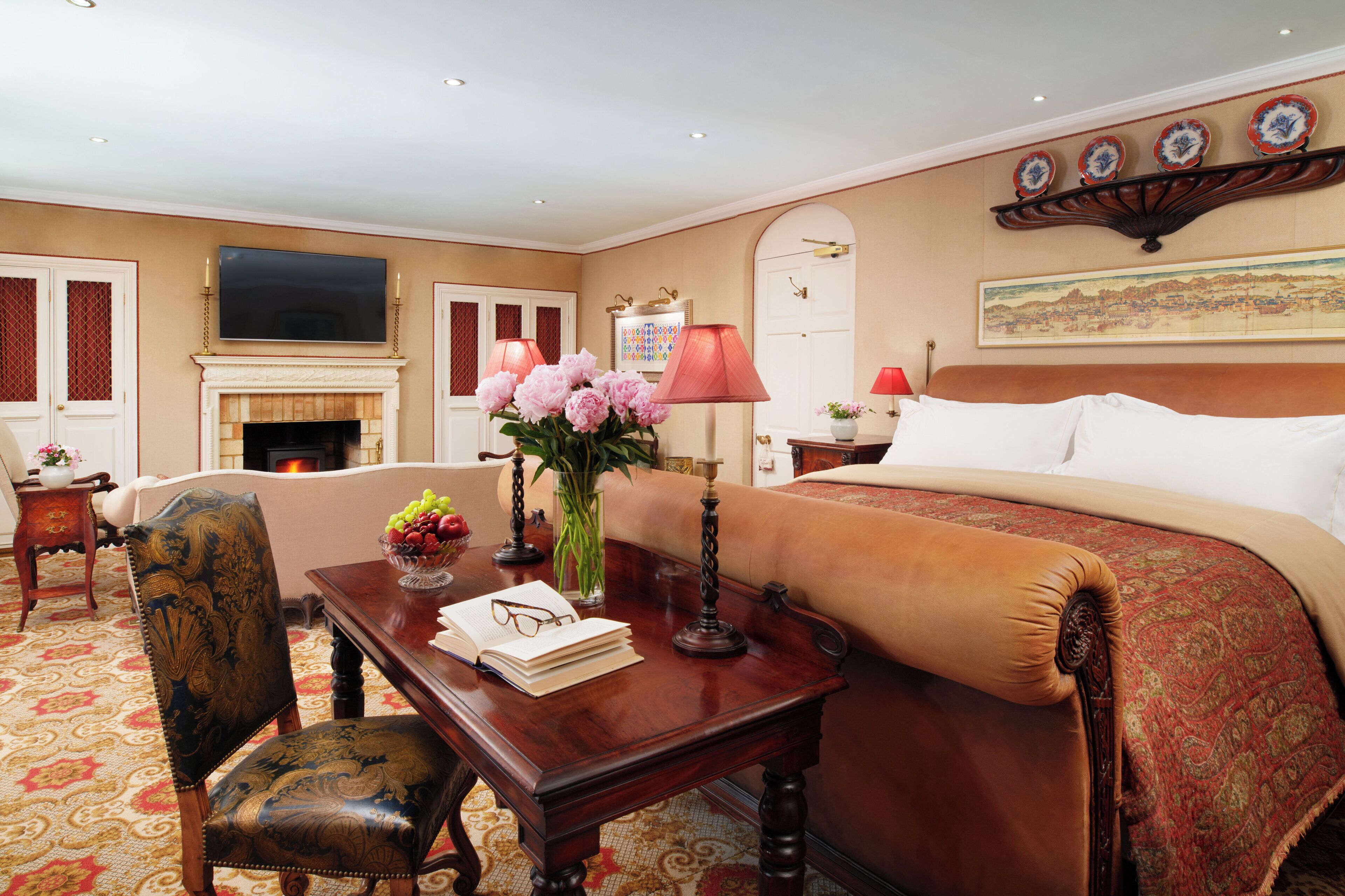 Una habitación de hotel con una cama grande, una zona de estar con una mesa y sillas, una chimenea y un televisor montado en la pared.