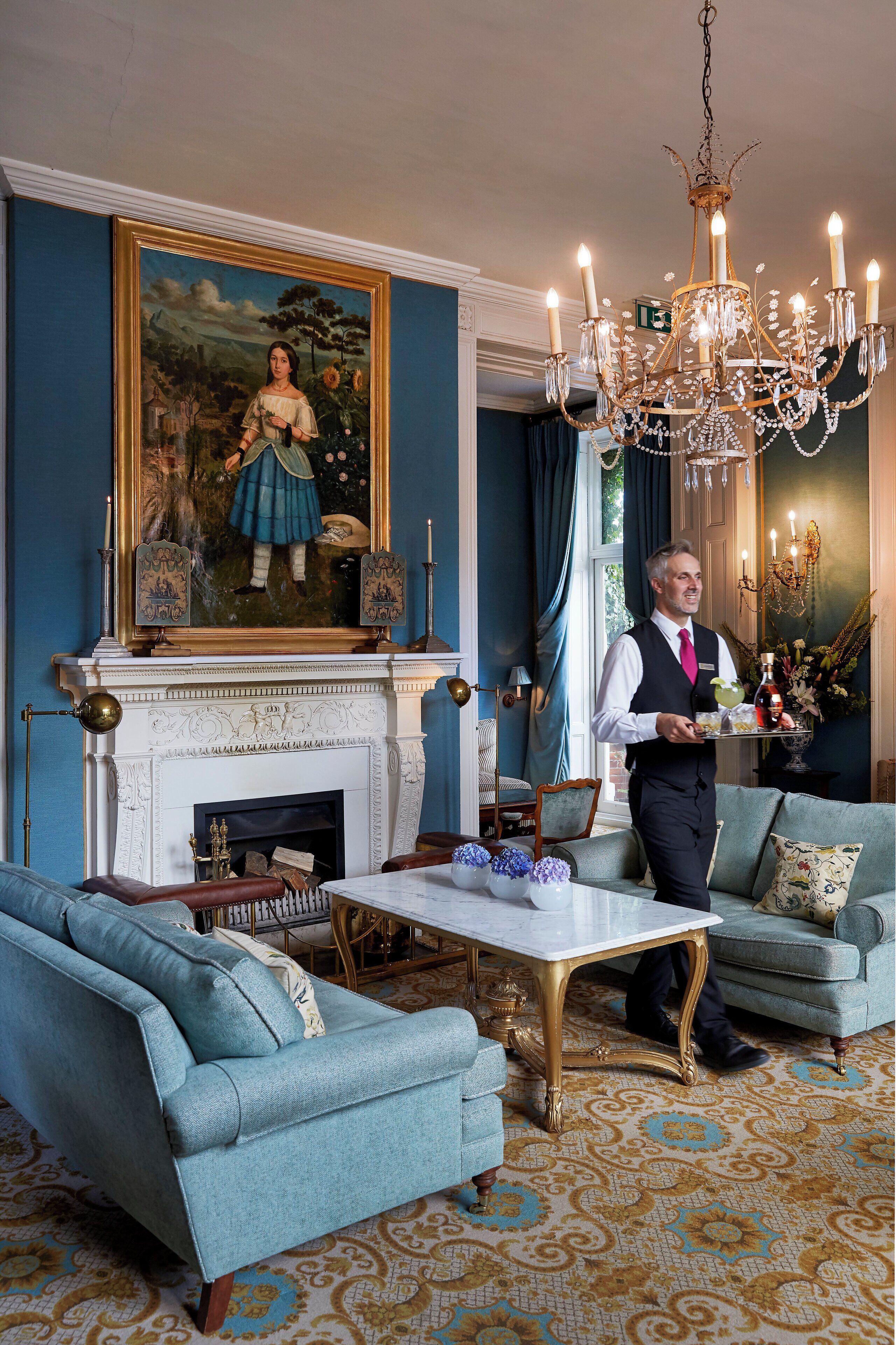 Een kamer met een open haard, een kroonluchter en een schilderij aan de muur.