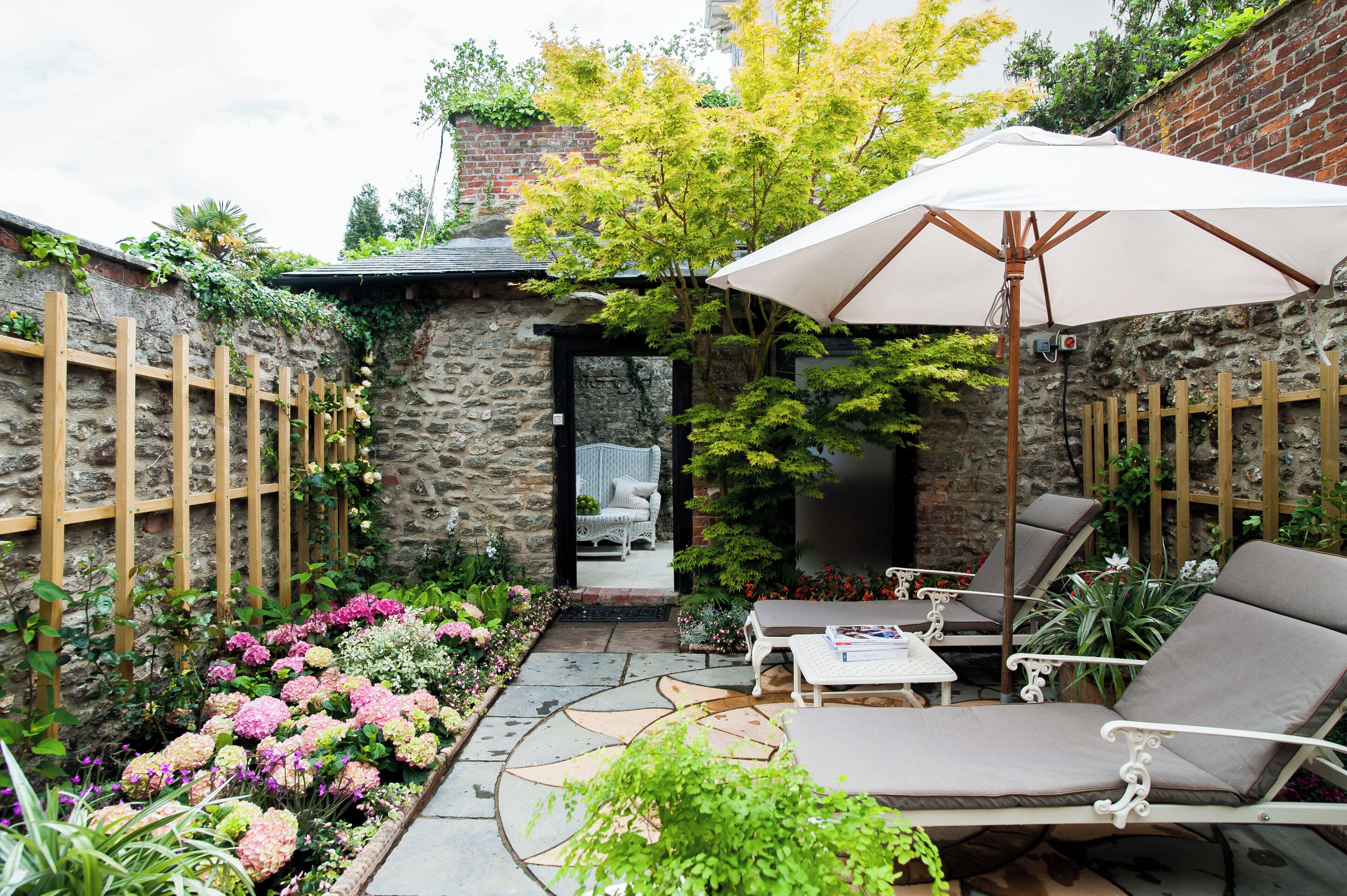 Un patio con muro de piedra, cerca de madera y zona de estar con mesa y sillas.