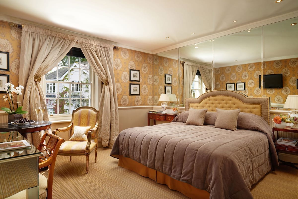 Une chambre bien aménagée, dotée d’un grand lit, d’un coin salon avec un fauteuil, d’un bureau et d’une fenêtre avec des rideaux.