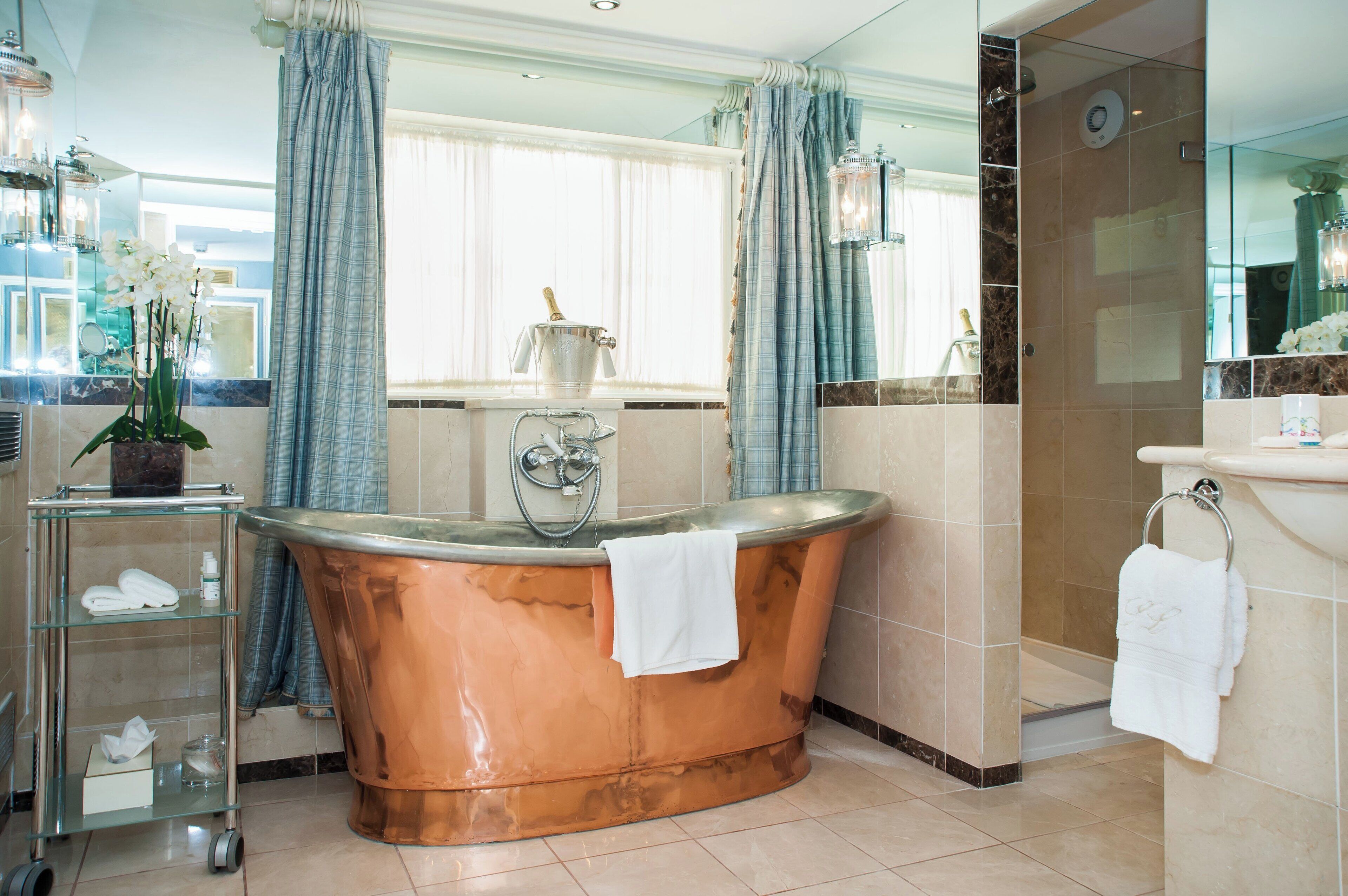 A modern bathroom with a freestanding copper bathtub, a glass shelf with toiletries, and a shower area.