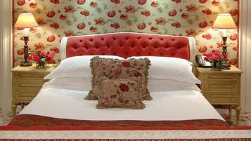 A neatly made bed with floral-patterned pillows and a red upholstered headboard. There are two bedside tables with lamps and a vase of flowers on each.
