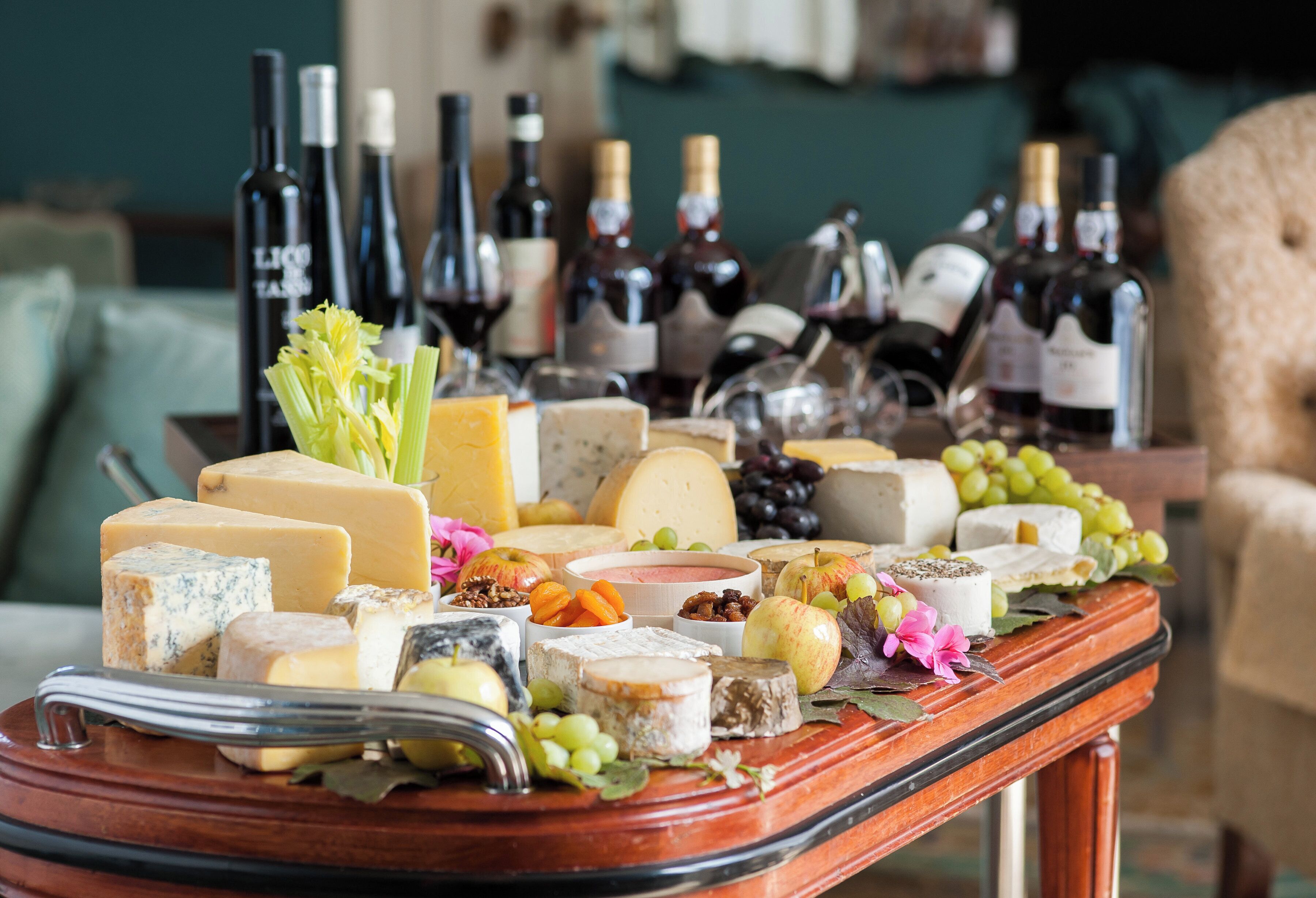 A cheese and wine board with various cheeses, grapes, and nuts, accompanied by wine bottles.
