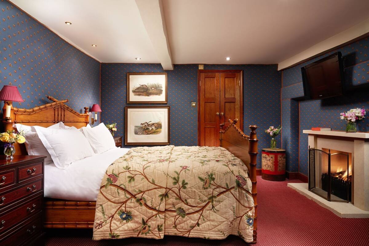 Une chambre à coucher comprenant un lit, une tête de lit en bois, une cheminée, une armoire en bois et un téléviseur fixé au mur.