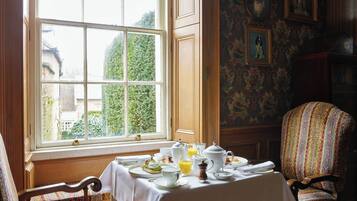 A dining area with a table set for breakfast, a window with a view of greenery, and a patterned wall with framed pictures.