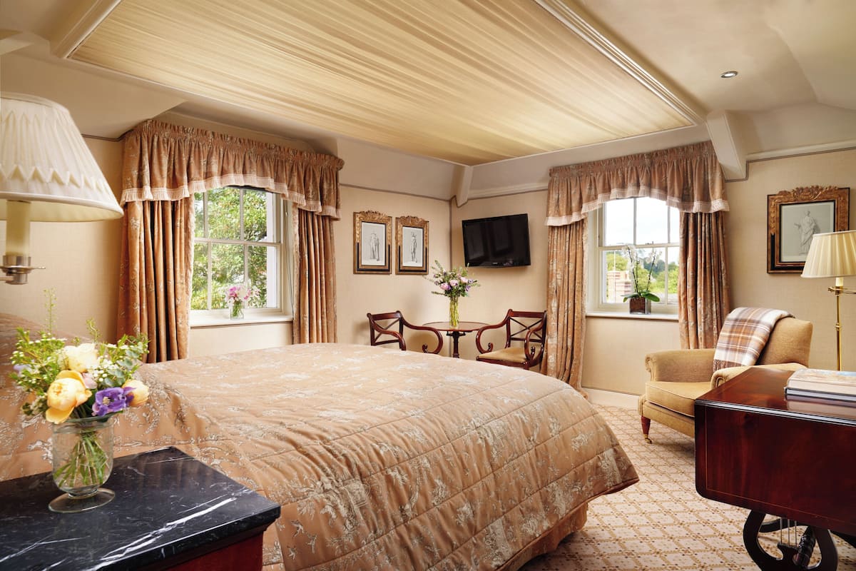 Une chambre d’hôtel avec un grand lit, un bureau avec une lampe, une chaise, un téléviseur et une fenêtre avec des rideaux.