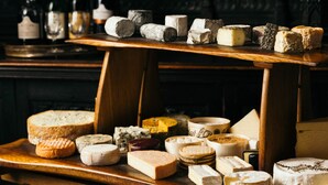 A variety of cheeses displayed on wooden tables in a dimly lit room with ornate wall decorations.