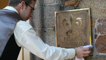 A man cleaning a brass plaque with a fleur-de-lis emblem and the words "RELAIS & CHATEAUX" on a stone wall.