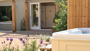 Un jacuzzi en un jardín con una pérgola de madera y una puerta que da a un porche cubierto.