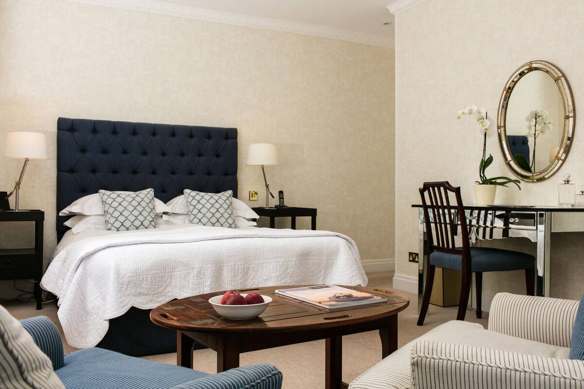 A hotel room with a large bed, two bedside tables, a desk with a chair, a round coffee table, and two armchairs.