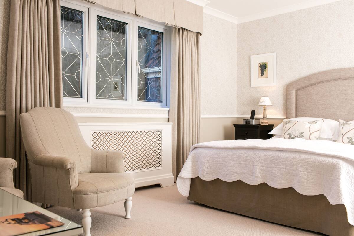 A bedroom with a bed, a chair, a nightstand, a lamp, and a window with curtains.
