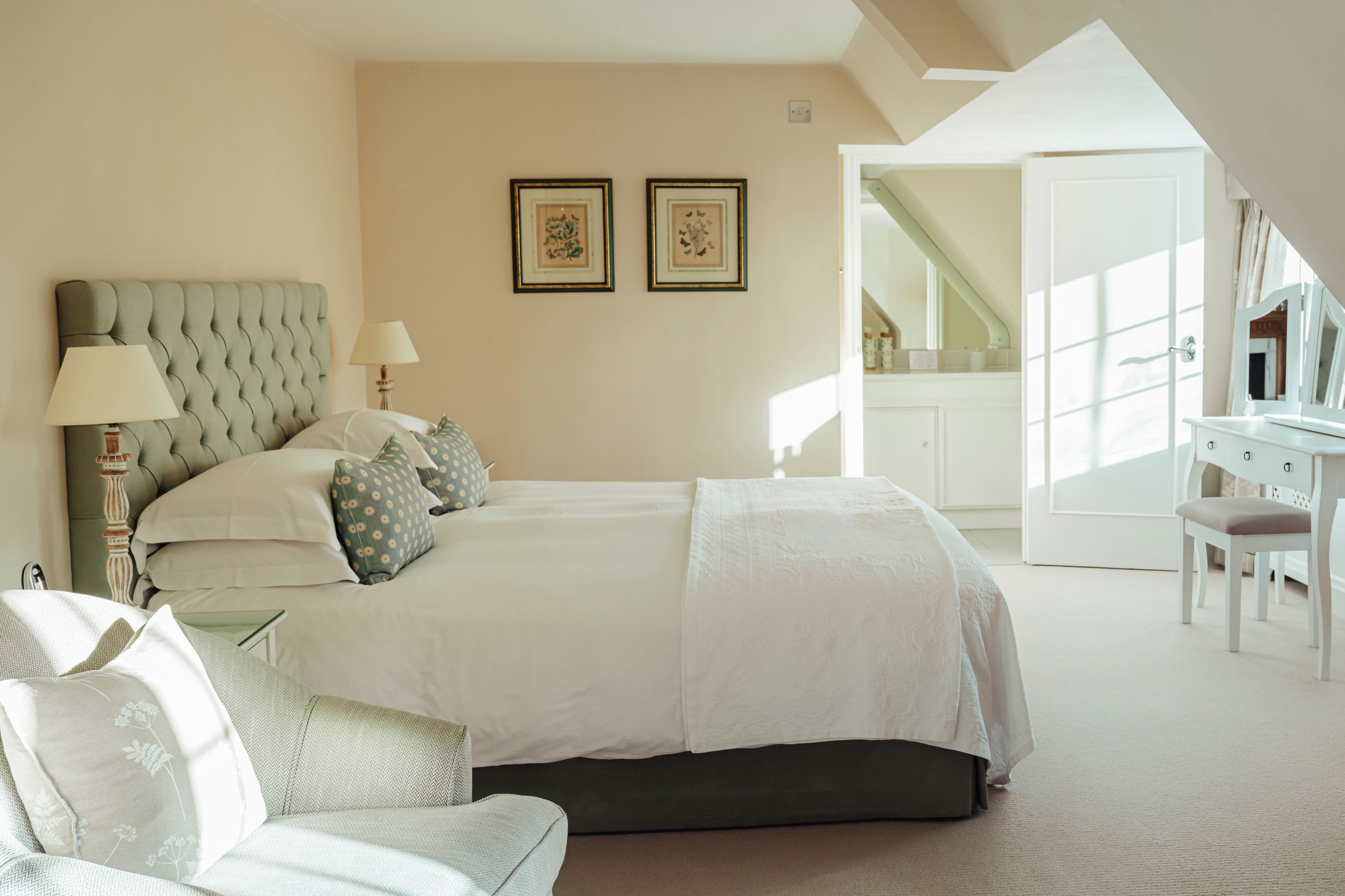 Une chambre avec un grand lit, un bureau et une chaise. Deux tableaux encadrés sont accrochés au mur.