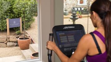 A woman using a stationary bike inside a room with a view of an outdoor garden area.