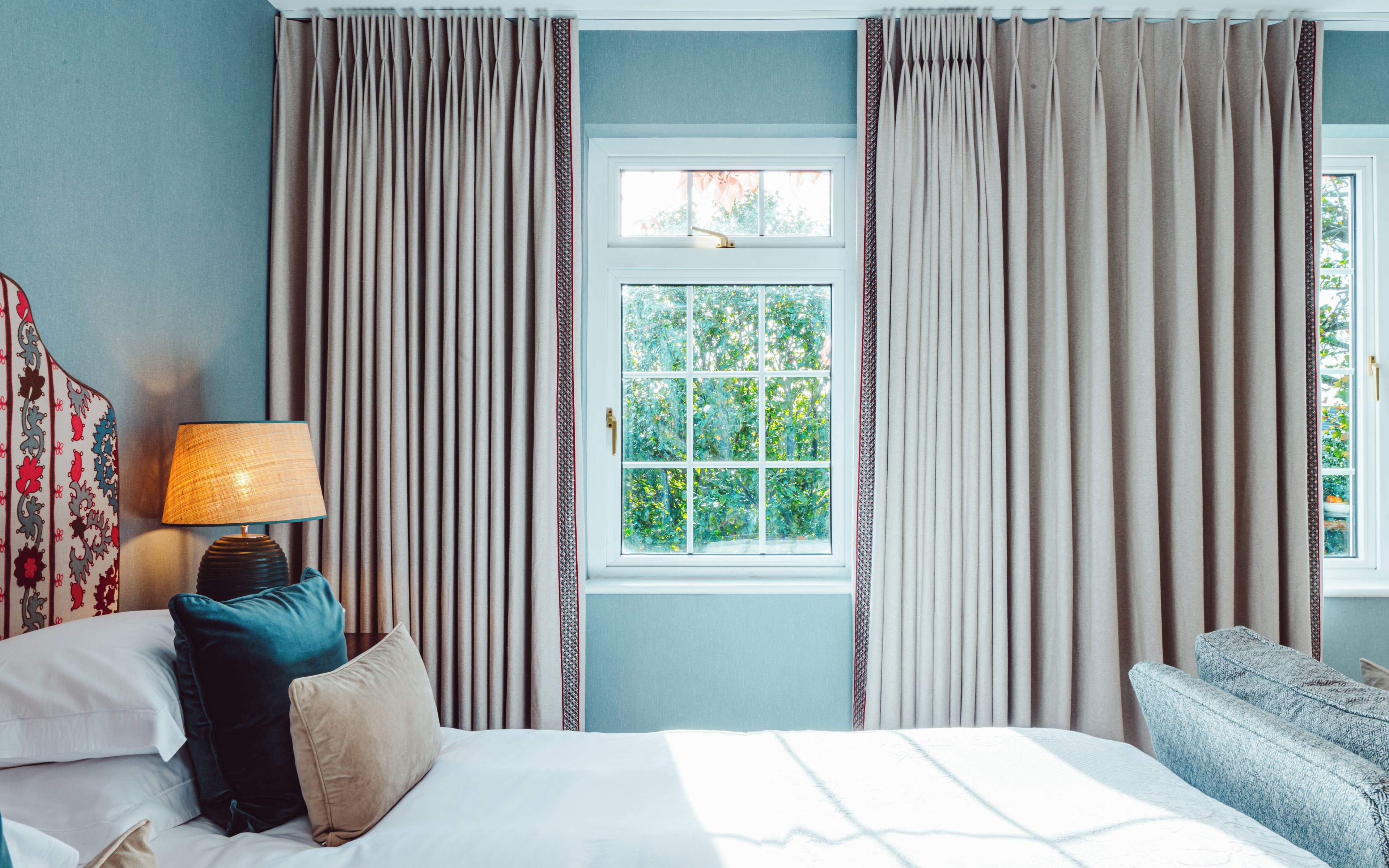 Une chambre d’hôtel avec un lit, une lampe de chevet, une fenêtre avec des rideaux et une vue sur la verdure.