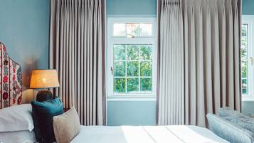 Une chambre d’hôtel avec un lit, une lampe de chevet, une fenêtre avec des rideaux et une vue sur la verdure.